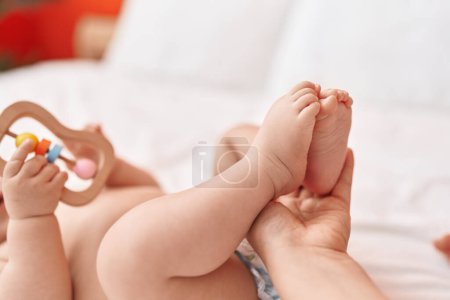 Téléchargez les photos : Adorable bambin hispanique couché sur le lit ayant massage des pieds dans la chambre - en image libre de droit