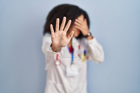 Photo for Young african american woman wearing doctor uniform and stethoscope covering eyes with hands and doing stop gesture with sad and fear expression. embarrassed and negative concept. - Royalty Free Image