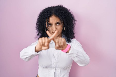 Téléchargez les photos : Hispanic woman with curly hair standing over pink background rejection expression crossing fingers doing negative sign - en image libre de droit