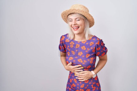 Photo for Young caucasian woman wearing flowers dress and summer hat smiling and laughing hard out loud because funny crazy joke with hands on body. - Royalty Free Image