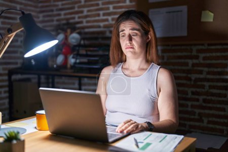 Photo for Brunette woman working at the office at night depressed and worry for distress, crying angry and afraid. sad expression. - Royalty Free Image