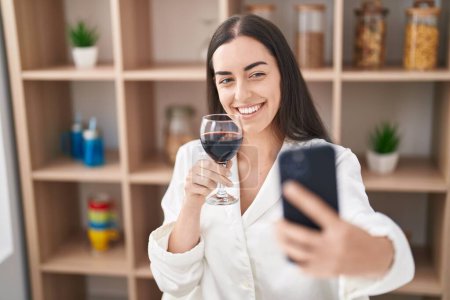 Téléchargez les photos : Young hispanic woman make selfie by the smartphone and drinking wine at home - en image libre de droit