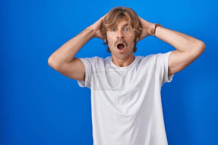 Photo for Middle age man standing over blue background crazy and scared with hands on head, afraid and surprised of shock with open mouth - Royalty Free Image