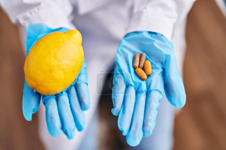 Téléchargez les photos : Jeune belle femme hispanique scientifique tenant du citron et des pilules au laboratoire - en image libre de droit