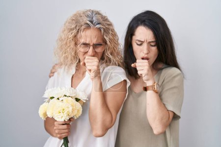 Foto de Madre e hija sosteniendo ramo de flores blancas sintiéndose mal y tosiendo como síntoma de resfriado o bronquitis. concepto de atención sanitaria. - Imagen libre de derechos
