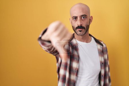 Photo for Hispanic man with beard standing over yellow background looking unhappy and angry showing rejection and negative with thumbs down gesture. bad expression. - Royalty Free Image