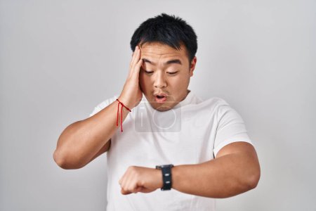 Téléchargez les photos : Young chinese man standing over white background looking at the watch time worried, afraid of getting late - en image libre de droit