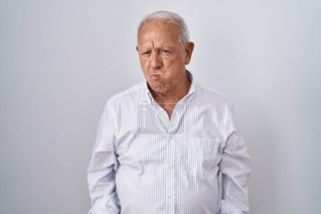 Téléchargez les photos : Senior man with grey hair standing over isolated background puffing cheeks with funny face. mouth inflated with air, crazy expression. - en image libre de droit