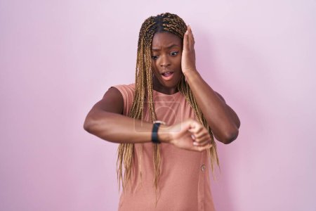 Téléchargez les photos : African american woman with braided hair standing over pink background looking at the watch time worried, afraid of getting late - en image libre de droit