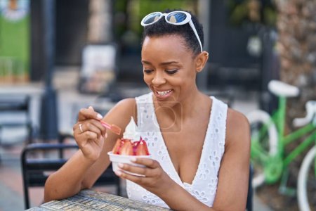 Photo for African american woman eating ice cream sitting on table at coffee shop terrace - Royalty Free Image