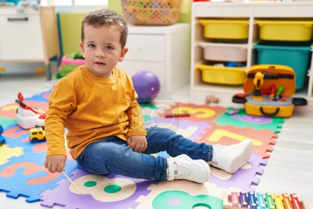 Foto de Adorable chico caucásico jugando xilófono sentado en el suelo en el jardín de infantes - Imagen libre de derechos