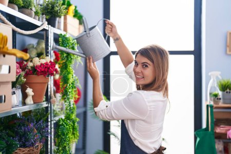 Téléchargez les photos : Jeune femme fleuriste souriant usine d'arrosage confiant au fleuriste - en image libre de droit