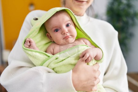 Téléchargez les photos : Adorable caucasian baby on mother arms wearing towel after shower at bedroom - en image libre de droit