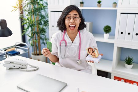 Photo for Young hispanic doctor woman holding anatomical model of uterus with fetus and birth control pills celebrating crazy and amazed for success with open eyes screaming excited. - Royalty Free Image