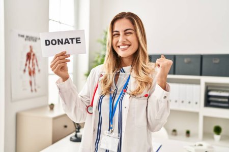 Téléchargez les photos : Young blonde doctor woman supporting organs donations screaming proud, celebrating victory and success very excited with raised arm - en image libre de droit