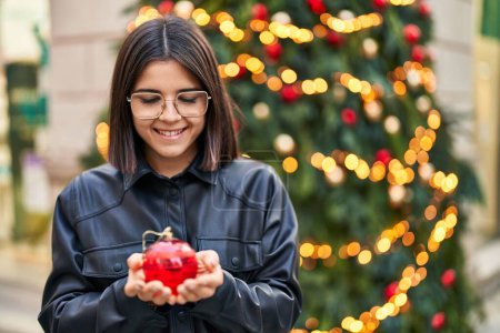 Photo for Young beautiful hispanic woman smiling confident holding christmas decor ball at park - Royalty Free Image
