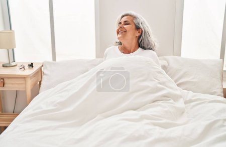 Téléchargez les photos : Femme d'âge moyen souriant confiant assis sur le lit dans la chambre - en image libre de droit
