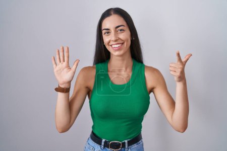 Foto de Mujer joven de pie sobre fondo aislado mostrando y señalando hacia arriba con los dedos número siete mientras sonríe confiado y feliz. - Imagen libre de derechos