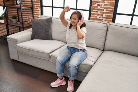 Foto de Síndrome de Down mujer escuchando música y bailando sentada en el sofá en casa - Imagen libre de derechos