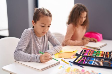 Téléchargez les photos : Deux élèves assis sur la table dessinent sur du papier pour ordinateur portable en classe - en image libre de droit