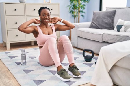 Téléchargez les photos : Afro-américaine femme souriant entraînement confiant abs exercice à la maison - en image libre de droit