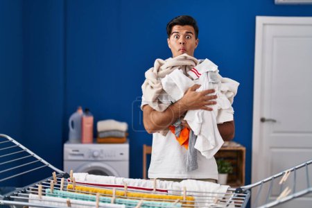 Foto de Hombre hispano colgando ropa en el tendedero haciendo cara de pez con boca y ojos entrecerrados, loco y cómico. - Imagen libre de derechos