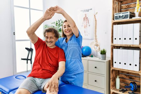 Foto de Hombre y mujer de mediana edad que usan uniforme de fisioterapia que tienen sesión de rehabilitación brazo de estiramiento en la clínica de fisioterapia - Imagen libre de derechos