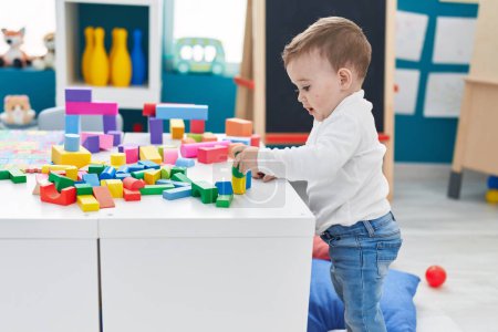 Foto de Adorable bebé caucásico jugando con bloques de construcción de pie en el jardín de infantes - Imagen libre de derechos