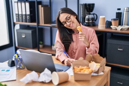 Photo for Young hispanic woman business worker eating delivery food working at office - Royalty Free Image