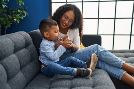 Téléchargez les photos : Mère et fils buvant un verre d'eau assis sur le canapé à la maison - en image libre de droit