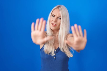 Photo for Caucasian woman standing over blue background doing stop gesture with hands palms, angry and frustration expression - Royalty Free Image