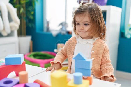 Téléchargez les photos : Adorable bambin blond jouant avec des blocs de construction debout à la maternelle - en image libre de droit