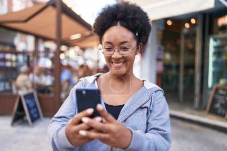 Téléchargez les photos : Femme afro-américaine souriante confiante en utilisant un smartphone sur la terrasse du café - en image libre de droit