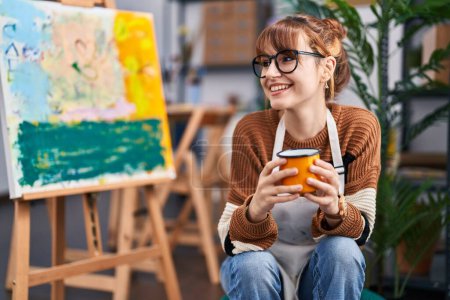 Téléchargez les photos : Jeune artiste souriante boire du café au studio d'art - en image libre de droit