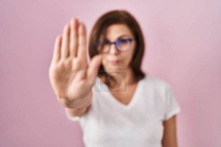 Photo for Middle age hispanic woman standing over pink background doing stop sing with palm of the hand. warning expression with negative and serious gesture on the face. - Royalty Free Image