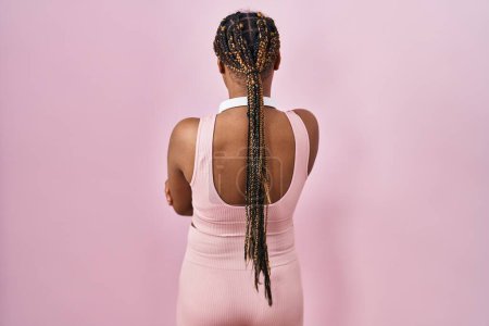 Foto de Mujer afroamericana con trenzas con ropa deportiva y auriculares mirando hacia atrás con los brazos cruzados - Imagen libre de derechos