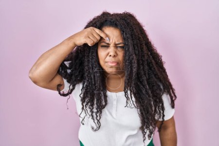 Téléchargez les photos : Plus size hispanic woman standing over pink background pointing unhappy to pimple on forehead, ugly infection of blackhead. acne and skin problem - en image libre de droit