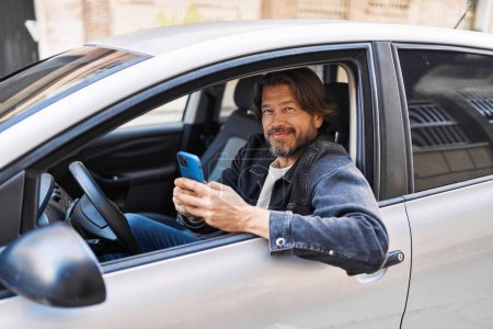Foto de Hombre de mediana edad usando teléfono inteligente sentado en el coche en la calle - Imagen libre de derechos