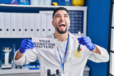 Photo for Young handsome man working at scientist laboratory holding blood sample angry and mad screaming frustrated and furious, shouting with anger looking up. - Royalty Free Image