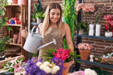Photo for Young beautiful hispanic woman florist watering plant at florist - Royalty Free Image