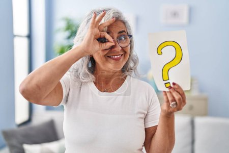 Téléchargez les photos : Middle age woman with grey hair holding question mark smiling happy doing ok sign with hand on eye looking through fingers - en image libre de droit