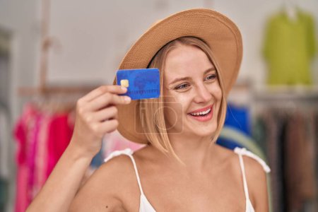 Téléchargez les photos : Jeune cliente blonde portant un chapeau d'été tenant une carte de crédit au magasin de vêtements - en image libre de droit