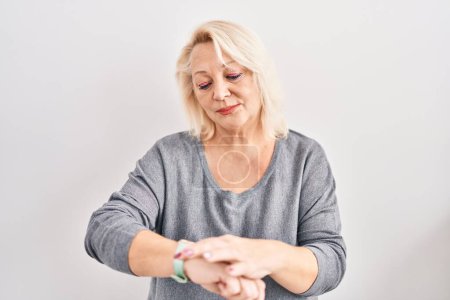 Foto de Mujer caucásica de mediana edad de pie sobre fondo blanco comprobar el tiempo en reloj de pulsera, relajado y seguro - Imagen libre de derechos