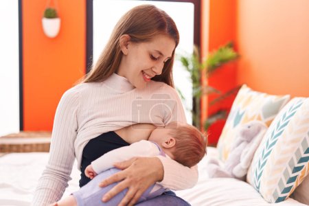 Foto de Madre e hijo sentados en la cama amamantando al bebé en el dormitorio - Imagen libre de derechos