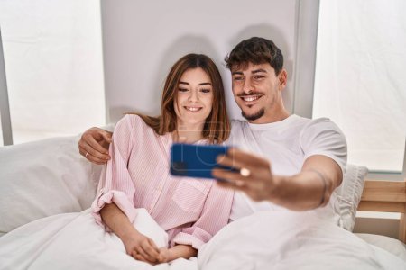 Foto de Mand and woman couple using smartphone sitting on bed at bedroom - Imagen libre de derechos