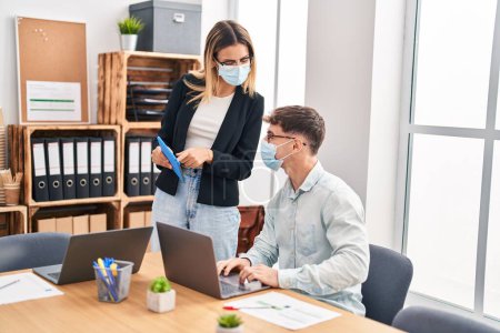Photo for Young man and woman business workers wearing medical mask using laptop and touchpad at office - Royalty Free Image