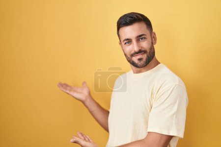 Foto de Hombre hispano guapo de pie sobre fondo amarillo invitando a entrar sonriente natural con la mano abierta - Imagen libre de derechos