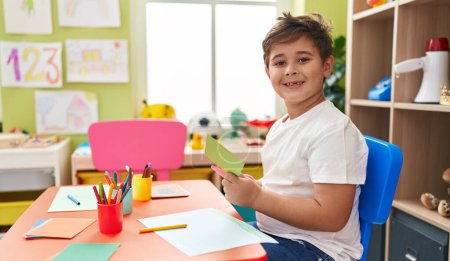Téléchargez les photos : Adorable hispanic boy student smiling confident cutting paper at kindergarten - en image libre de droit
