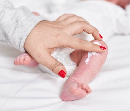 Foto de Adorable caucasian baby lying on bed applying lotion on leg at bedroom - Imagen libre de derechos