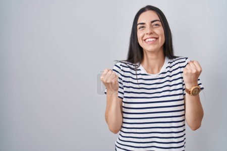 Téléchargez les photos : Young brunette woman wearing striped t shirt very happy and excited doing winner gesture with arms raised, smiling and screaming for success. celebration concept. - en image libre de droit